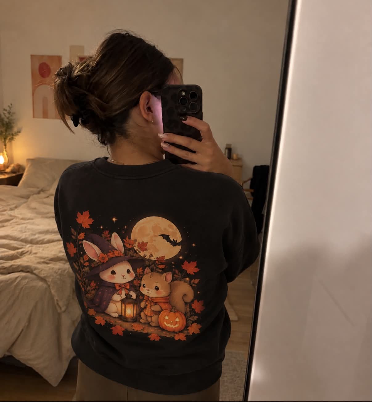 Selfie de dos au miroir, sweat noir illustré dans le dos d’un lapin-sorcière et d’un écureuil sous la pleine lune.