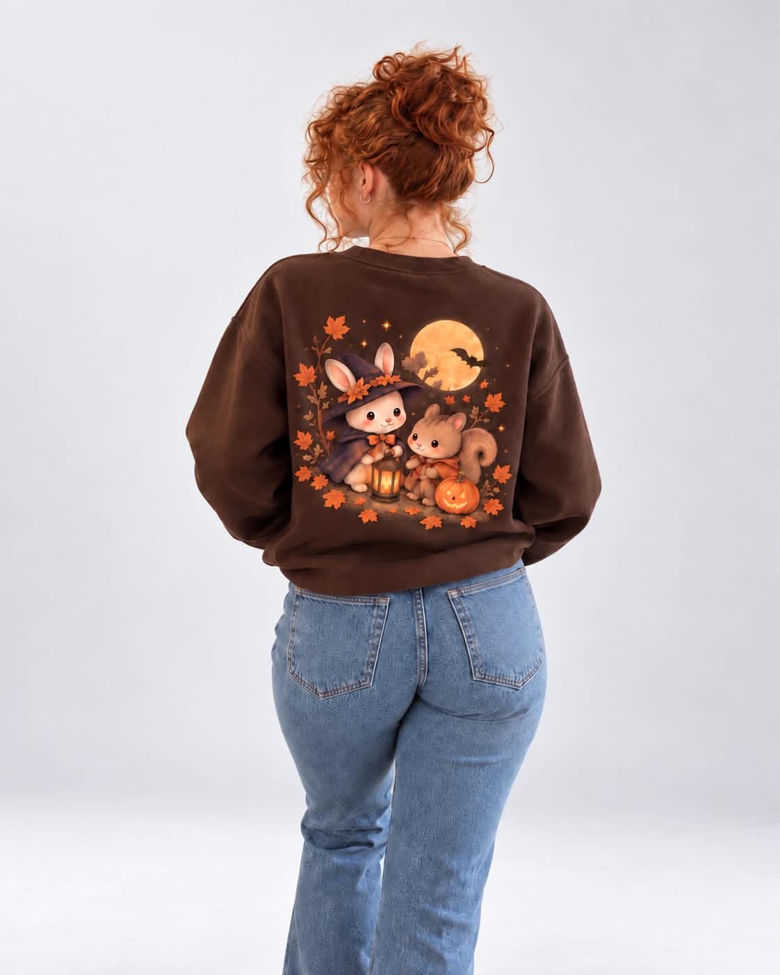 Le sweat chocolat porté de dos : le lapin-sorcière et l’écureuil sous la pleine lune, entourés de feuilles d’automne.